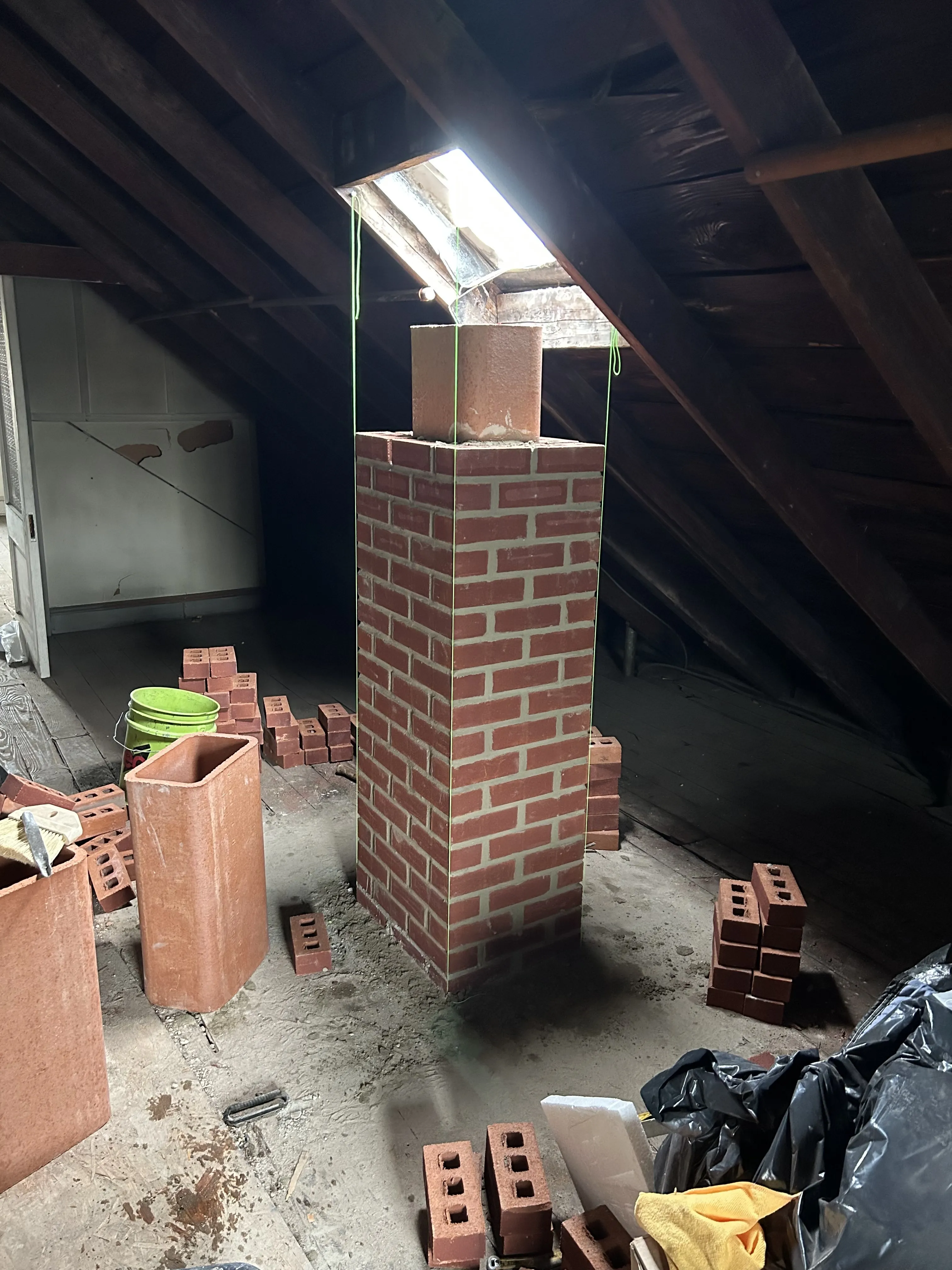 Rebuilt brick chimney shaft rising through the attic, with the new flue liner set and extra brick on hand.