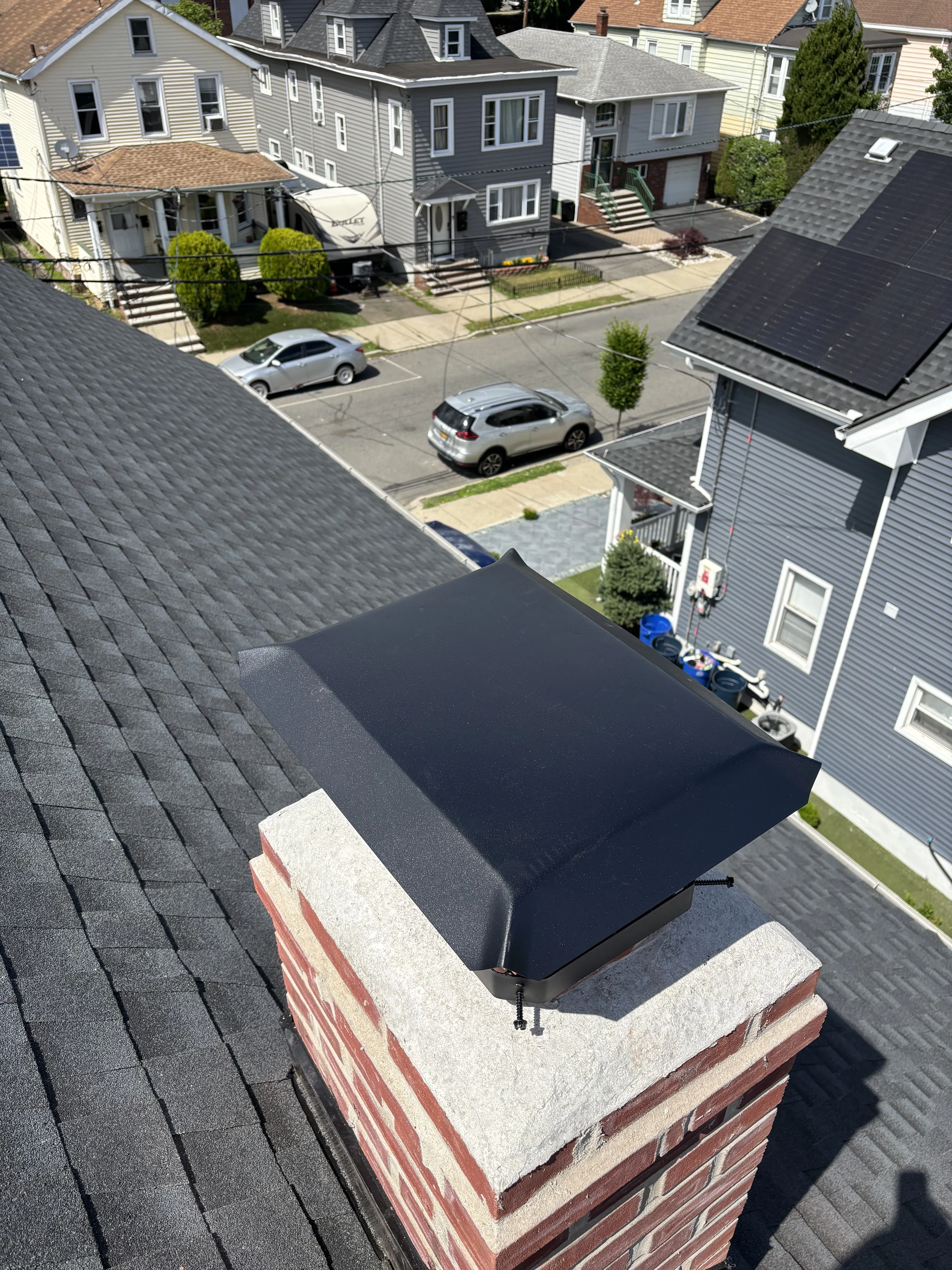 New black metal flashing wrapping the base of the brick chimney against the new shingle roof.