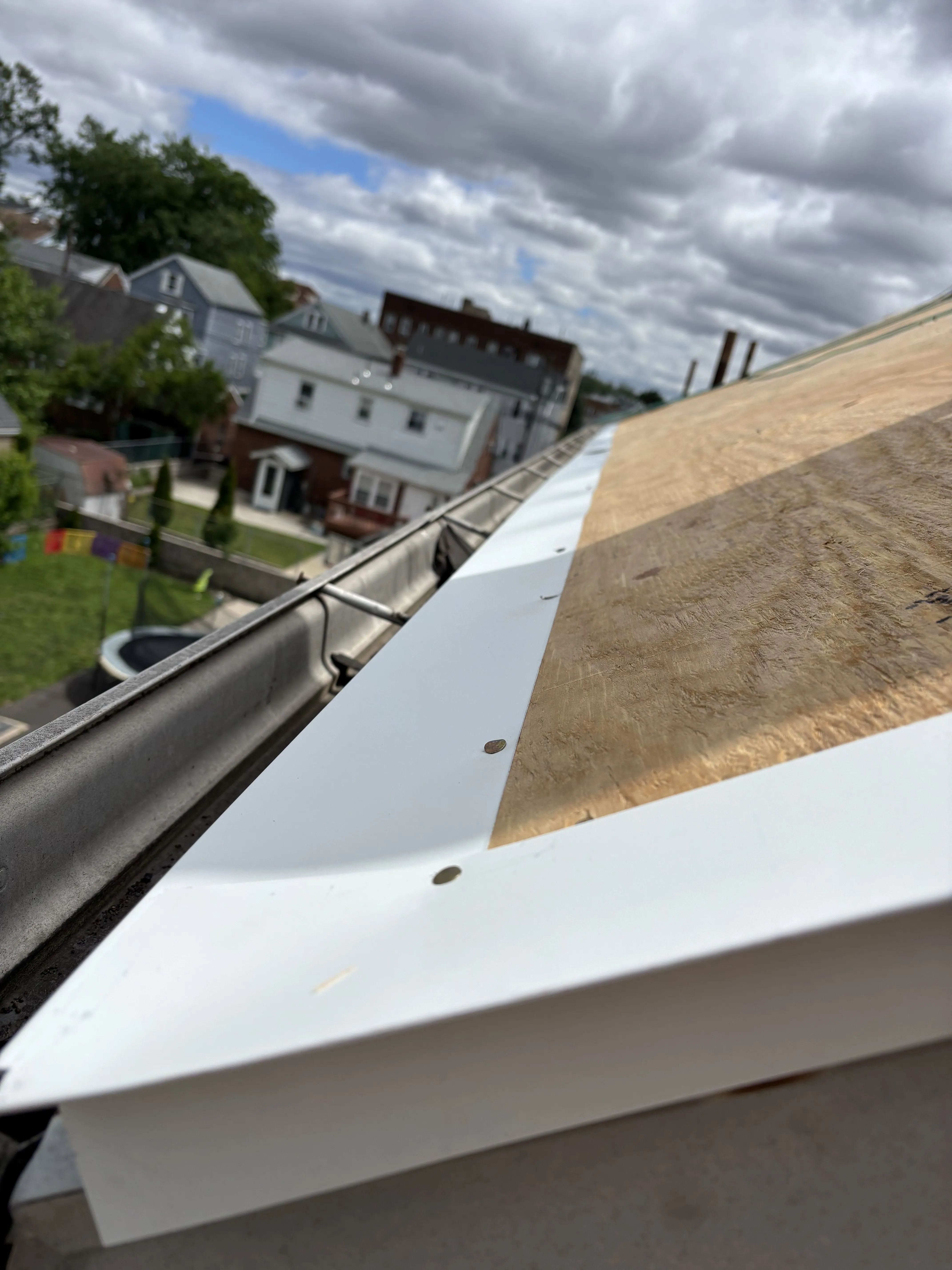 New plywood roof decking and white drip-edge metal installed along the eave, replacing the old roof edge.