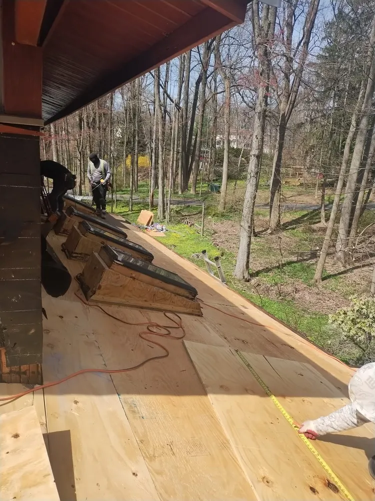 Crew measuring and laying new plywood decking after tearing off the old roof and skylight curbs.