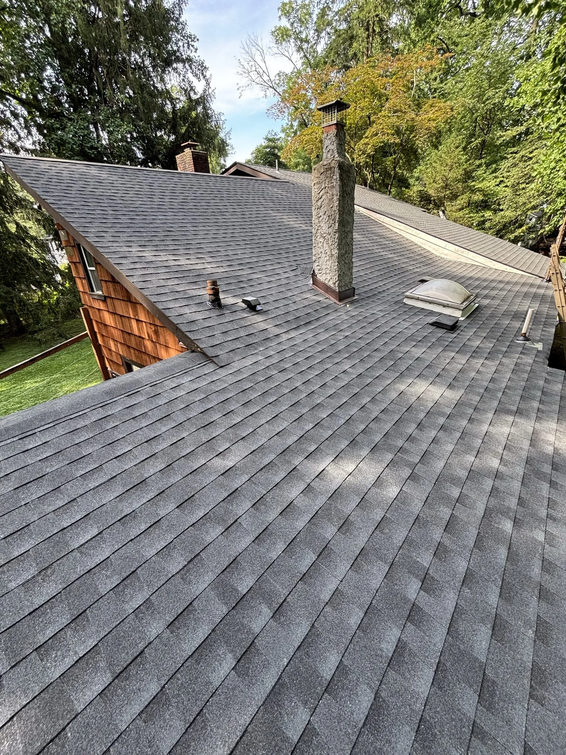 The same roof finished in new shingles with new vents, woods rising behind the house.