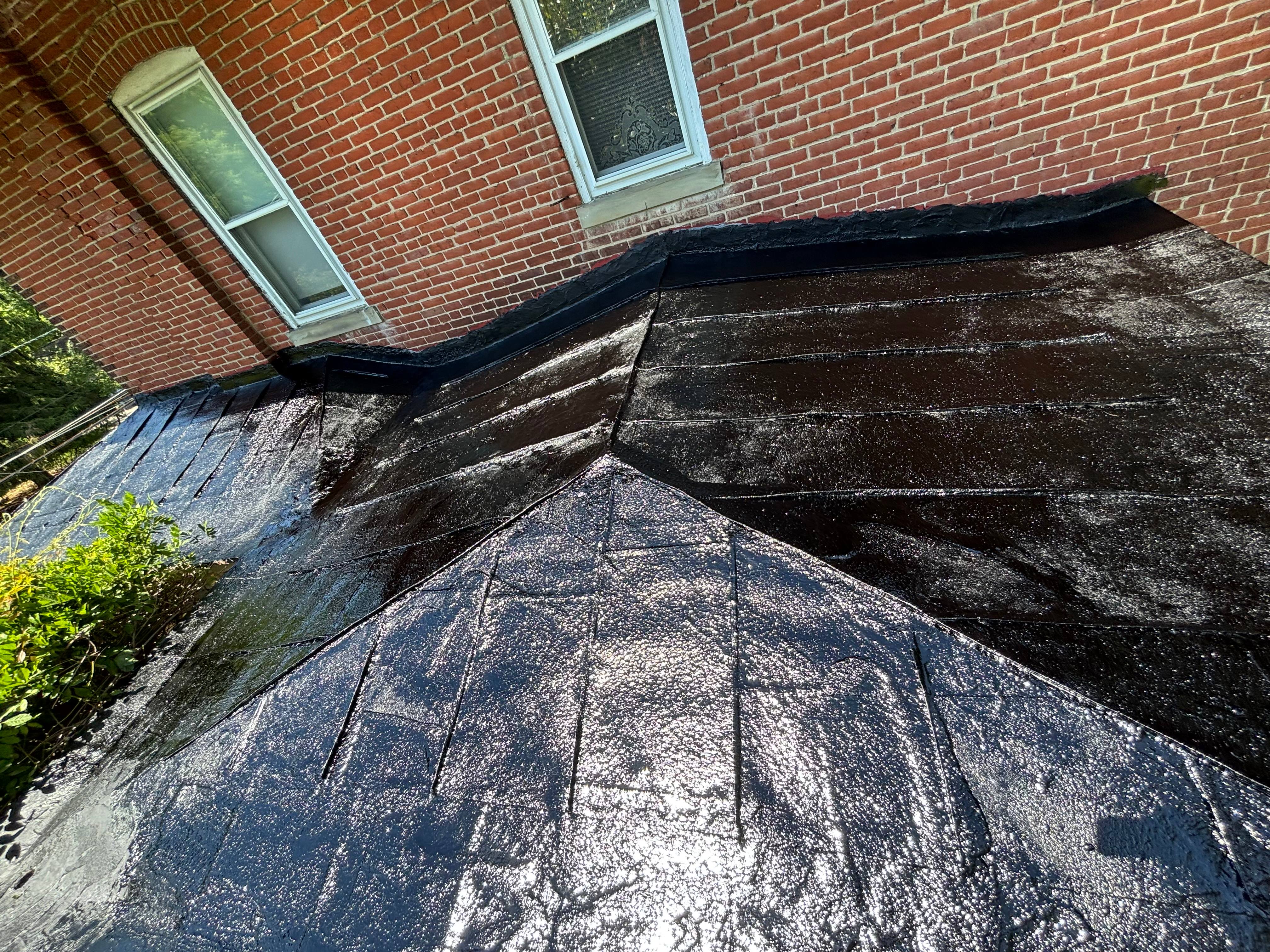 Finished flat metal roof in Lawrence Township coated glossy black, the planes meeting cleanly at the brick house.