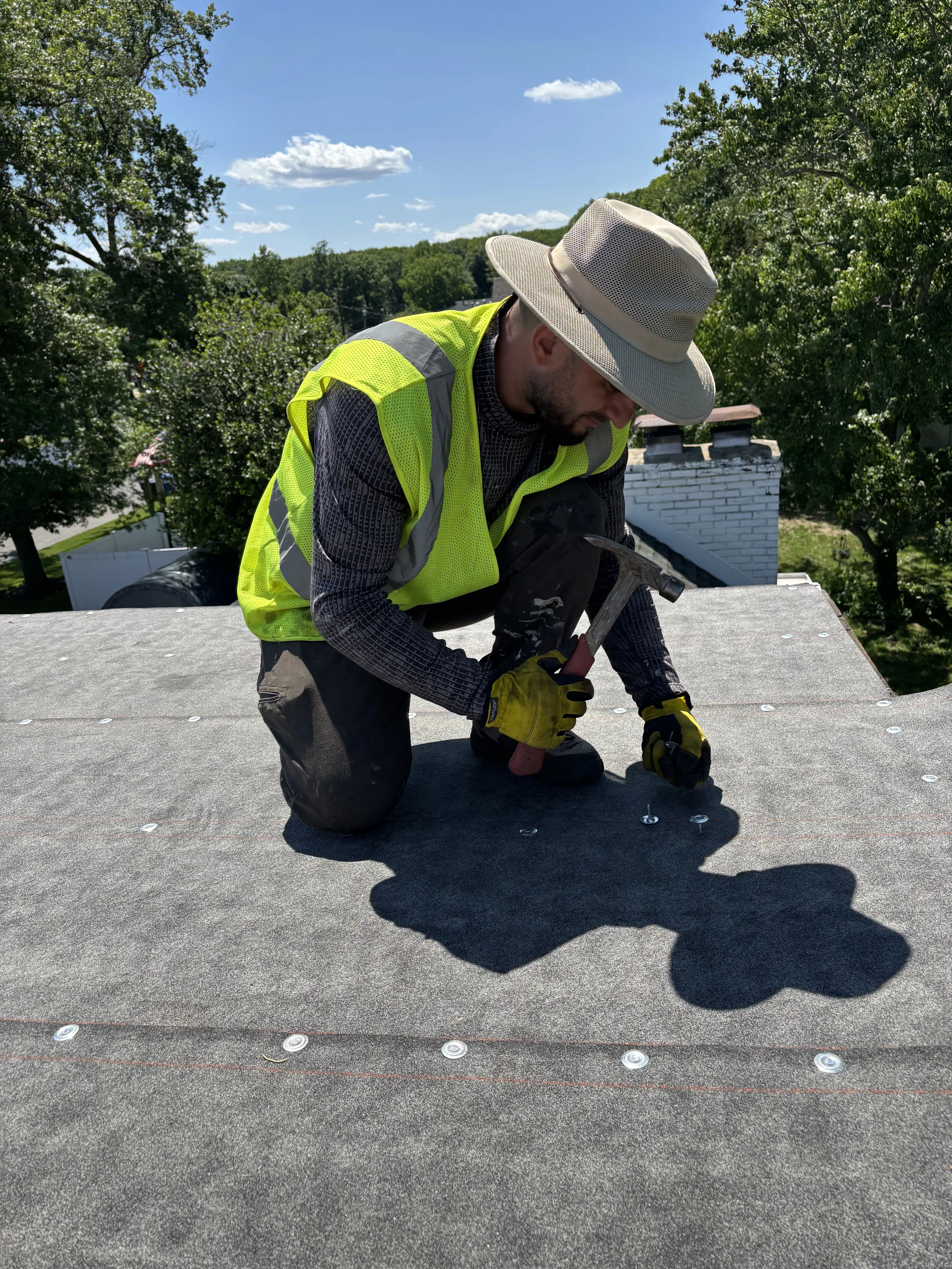 Roofer installing the flat-roof system over the new decking, rolling and fastening the membrane in place.