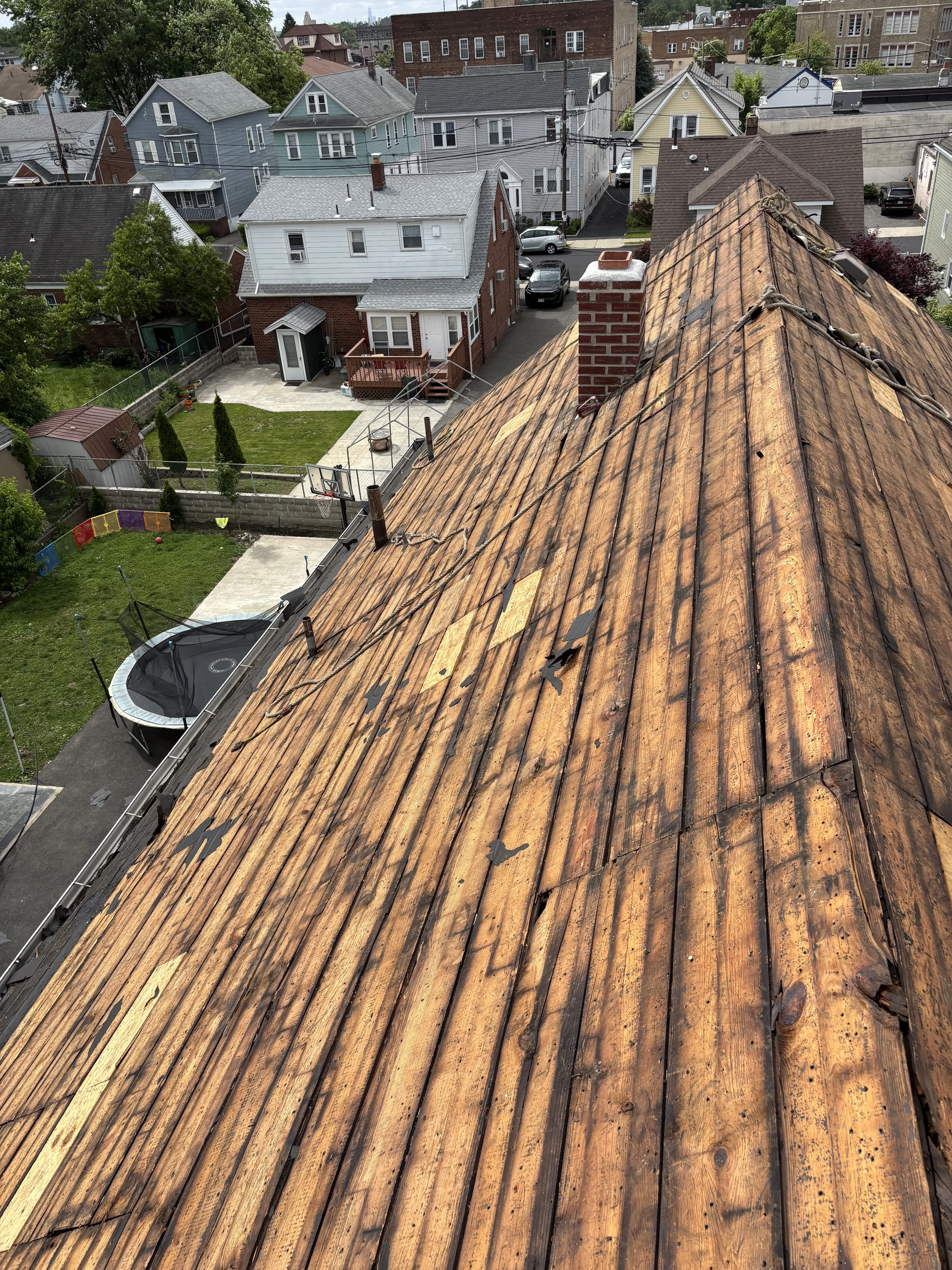 Old roofing torn off to the original wood plank decking, looking down the roof slope toward neighboring homes and street.